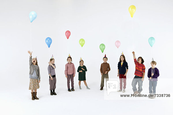 Eine Gruppe von meist gelangweilt aussehenden Kindern mit Ballons und Partyhüten
