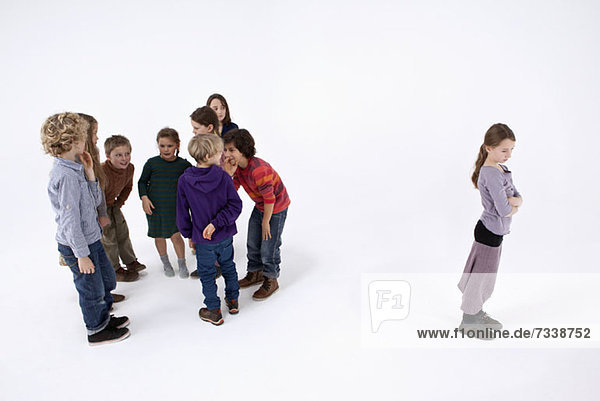 Ein Mädchen  das allein steht  die Arme verschränkt  während eine Gruppe von Kindern über sie klatscht.