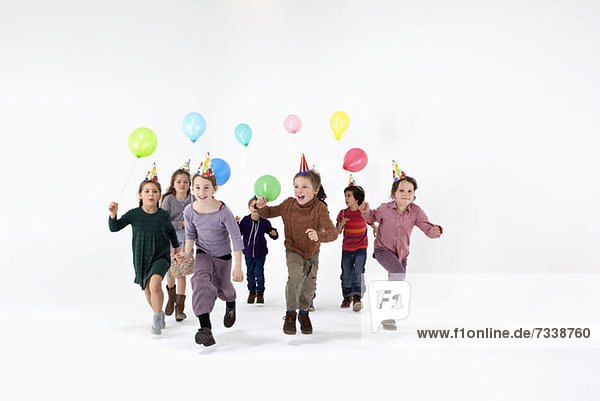 Eine Gruppe von Kindern mit Partyhüten und Luftballons  die vorwärts rennen.