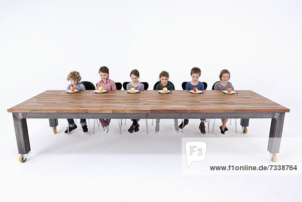 Sechs Kinder schauen unsicher auf die Äpfel auf dem Teller.