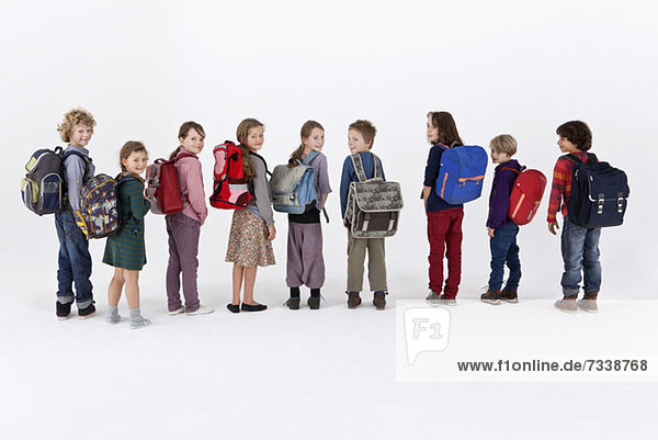 Eine Reihe von Schulkindern  die Rucksäcke tragen und in einer Reihe stehen.