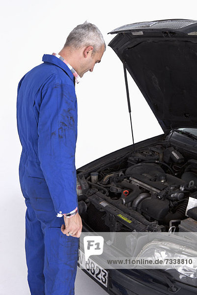 An auto mechanic looking under the hood of a car thoughtfully