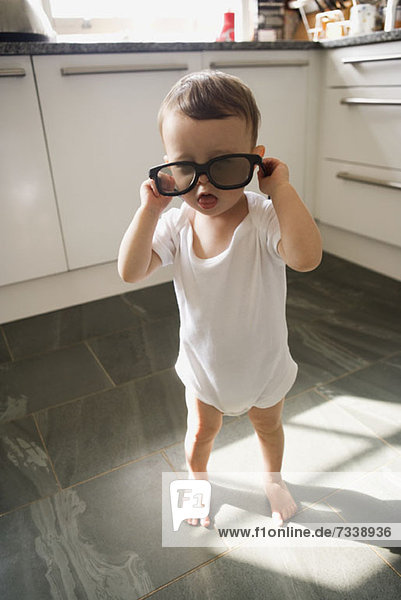 Ein Junge steht in einer häuslichen Küche und spielt mit einer Sonnenbrille.