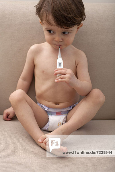 Ein Junge hält ein Thermometer im Mund.