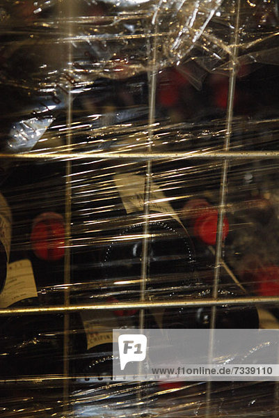 A metal crate filled with stacked red wine bottles and wrapped in plastic wrap
