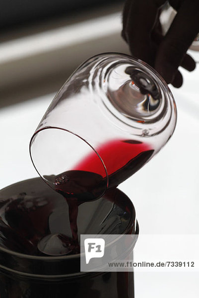 Eine Person  die bei einer Weinprobe Rotwein aus einem Weinglas in einen Spucknapf gießt.