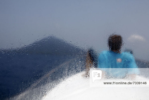 Ein auf einem Boot liegender Mann mit Blick auf den Vulkan Krakatau  Rückansicht  durchs Fenster gesehen