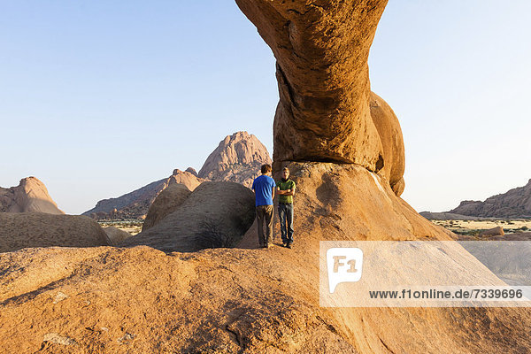 Zwei junge Männer unter Bogenfels  Spitzkoppe-Umgebung  Damaraland  Namibia  Afrika
