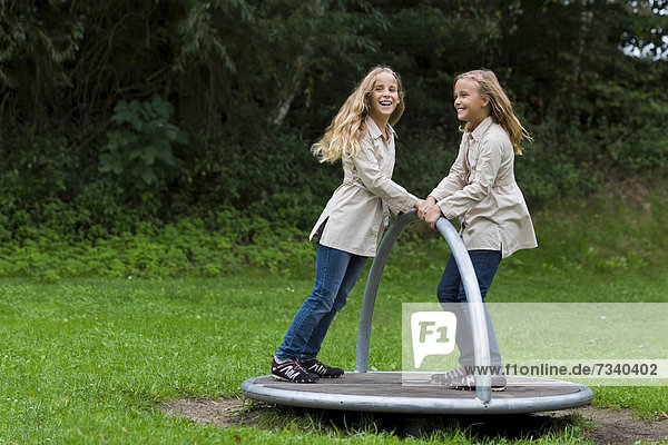 Zwillinge  Mädchen  9 Jahre  drehen sich auf dem Spielplatz mit einem Karussell