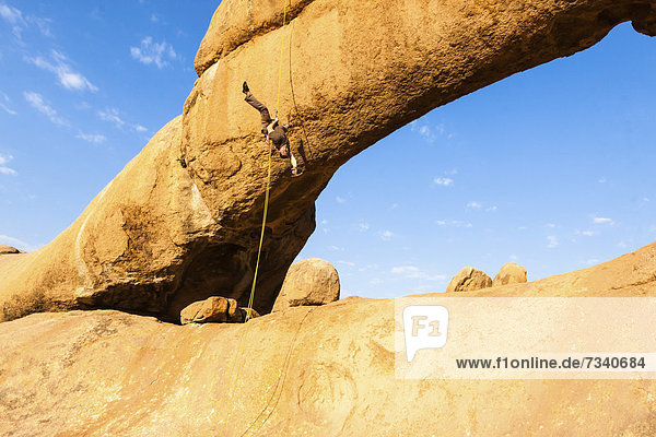 Junger Mann hängt kopfüber beim Abseilen vom Bogenfels  Spitzkoppe-Gebiet  Damaraland  Namibia  Afrika