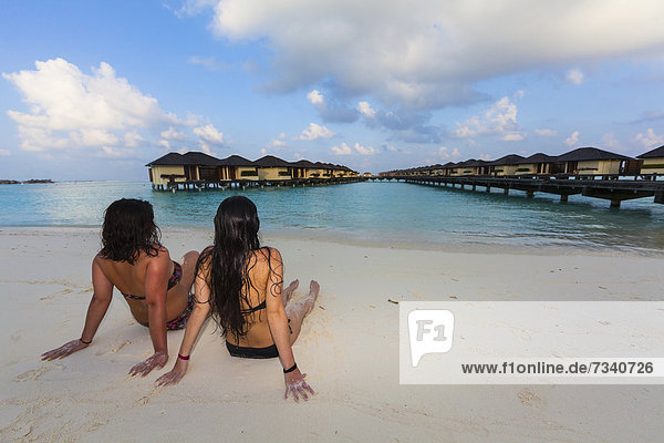 Two girls  about 15 and 19 years old sitting on the beach  lagoon  Paradise Island at the back  Lankanfinolhu  North Male Atoll  Republic of Maldives  Indian Ocean  Asia