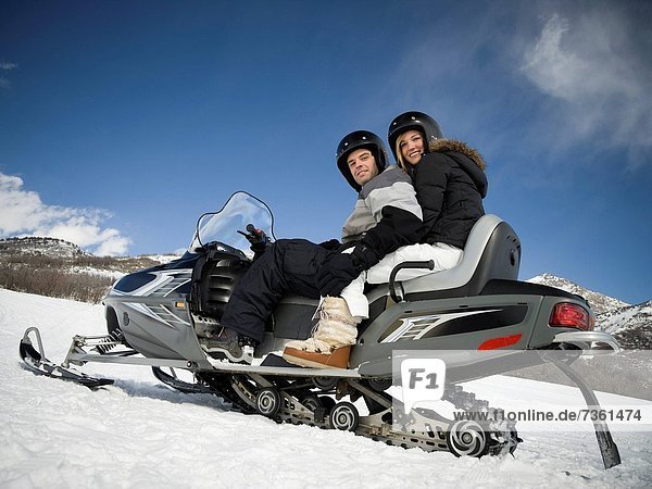 Low angle view of a young couple sitting on a snowmobile