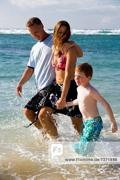 Couple with young boy walking in water on beach