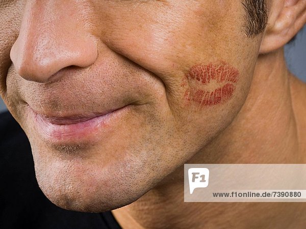 Closeup of man smiling with lipstick kiss on cheek