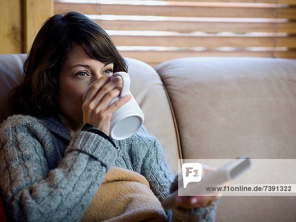 Woman on sofa with coffee mug and remote