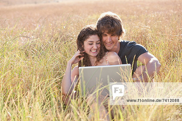 Paar mit Laptop im hohen Gras
