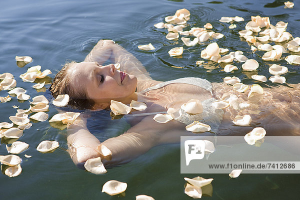 Frau schwimmt in Blütenblättern im stillen See