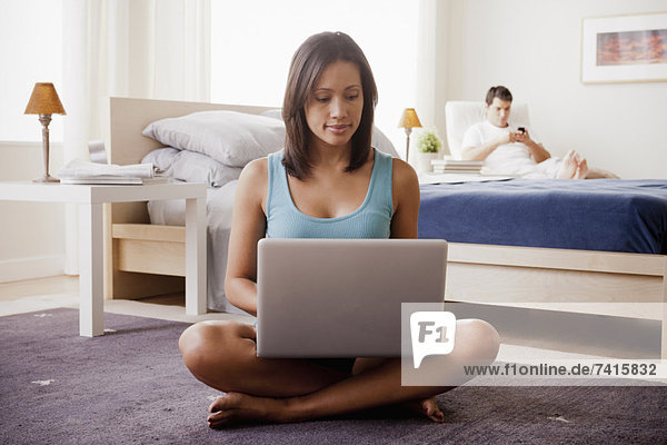 Woman using laptop with husband on lounger in background