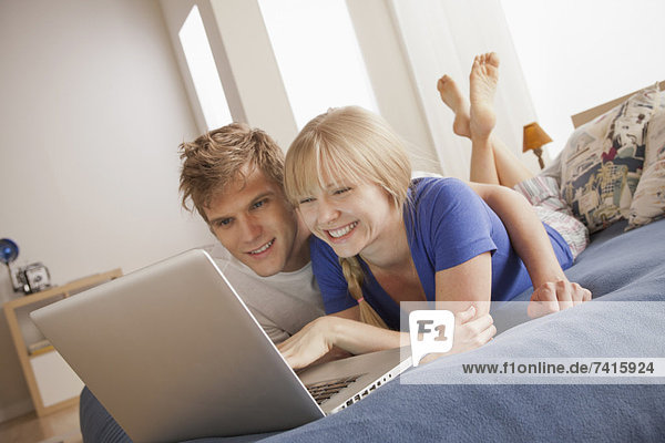 Happy couple lying on bed using laptop