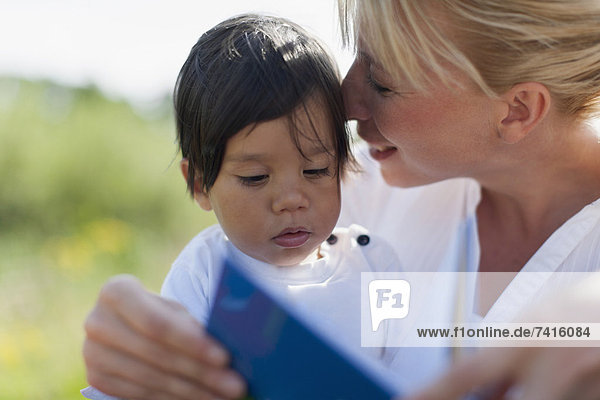 Mother reading book to her baby boy outdoors