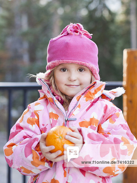 Girl (4-5) wearing warm clothing holding orange outdoors