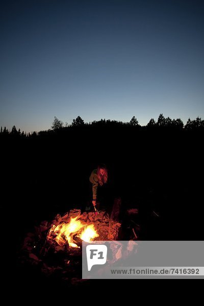A girl with a headlamp stands next to a campfire.