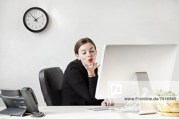 Studio shot of young woman blowing a kiss to computer monitor