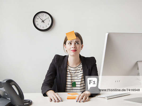 Studio shot of young woman working in office with adhesive note on her forehead