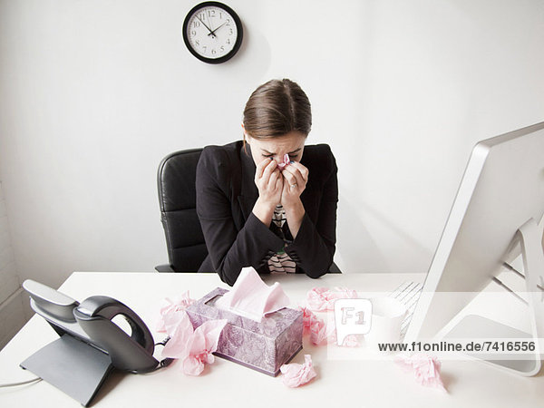Studio shot of young woman working in office sneezing