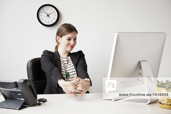Studio shot of young woman working in office and stretching her arms