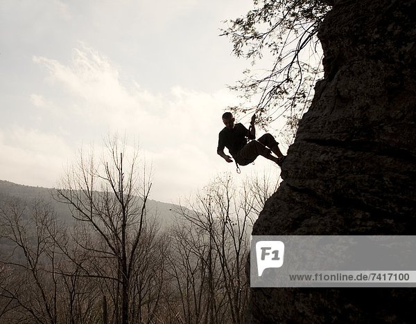 A rock climber is silhouetted against the sky as he rappels down the side of a cliff.