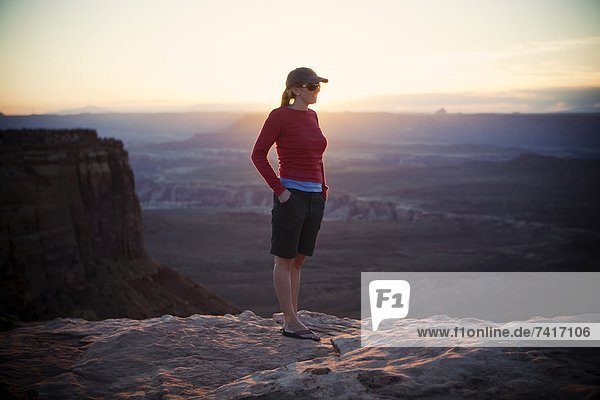 A young woman looks out at a view in Canyonlands National Park at sunset.