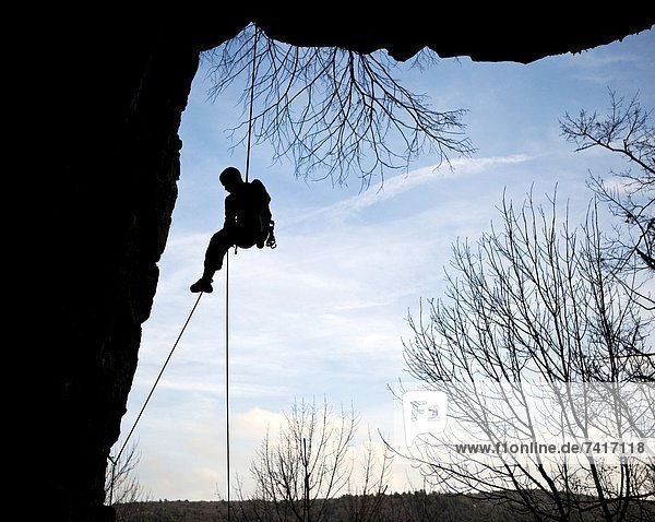 A climber rappels down from the side of a cliff (silhouette).