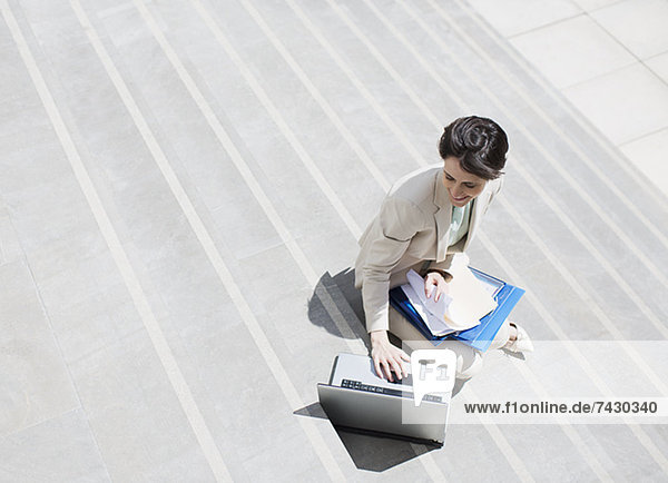 Geschäftsfrau mit Papierkram mit Laptop auf Stadttreppe