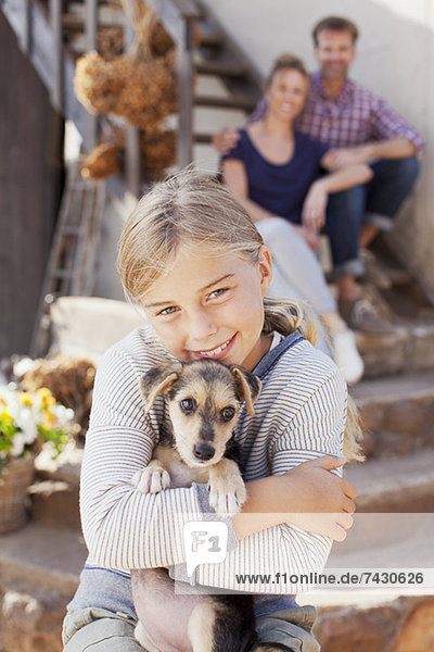 Portrait of smiling girl holding puppy with parents in background