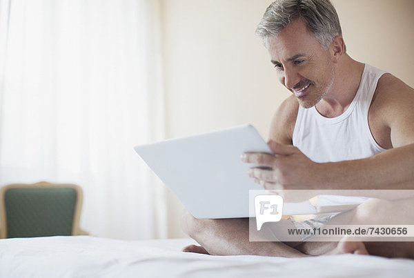 Lächelnder Mann mit Laptop im Bett