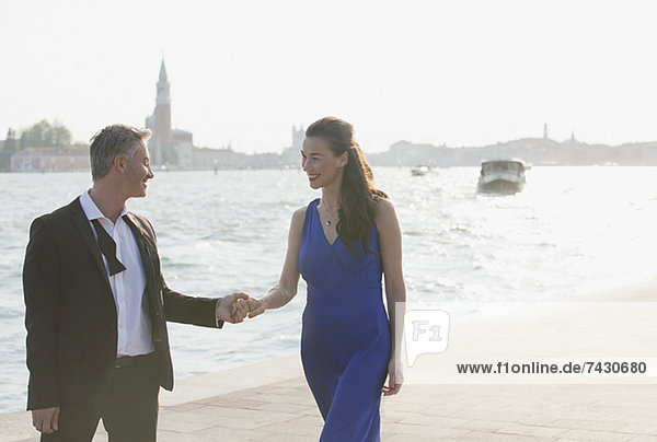 Gut gekleidetes Paar hält sich am Wasser in Venedig an den Händen