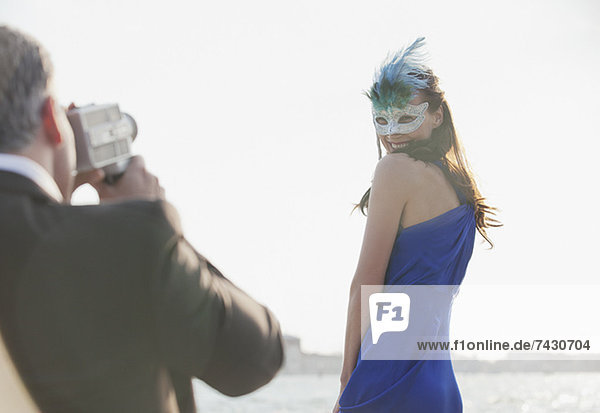 Mann filmt Frau mit Maske am Wasser in Venedig