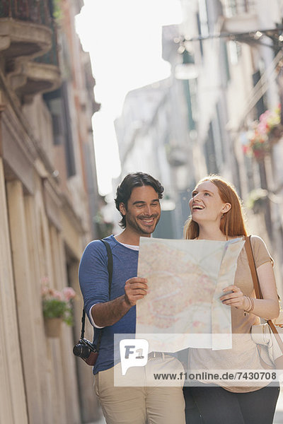 Smiling couple walking with map on narrow street in Venice