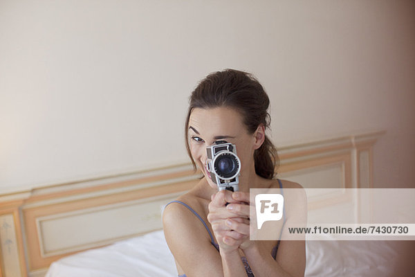 Porträt einer Frau  die eine altmodische Videokamera im Bett hält.