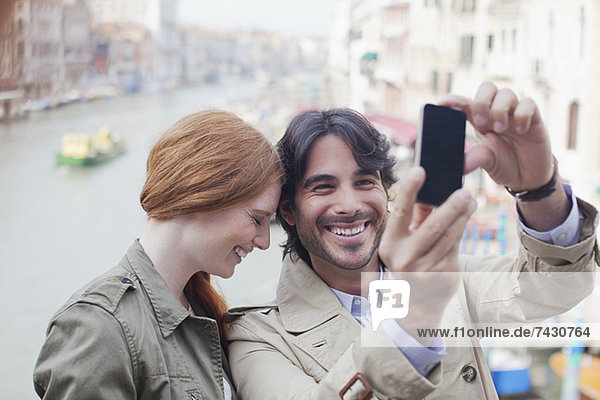 Lachendes Paar beim Selbstporträt mit Fotohandy am Kanal in Venedig