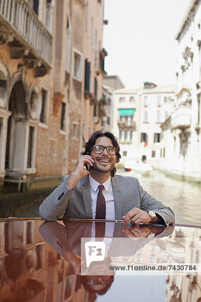 Smiling businessman talking on cell phone and riding boat through canal in Venice