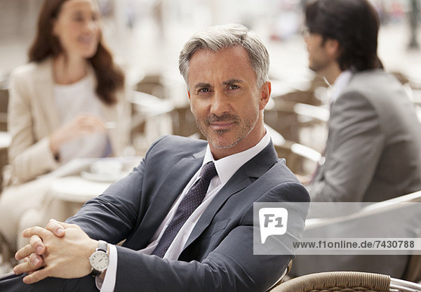 Porträt eines lächelnden Geschäftsmannes im Straßencafé mit Mitarbeitern im Hintergrund