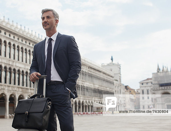 Selbstbewusster Geschäftsmann mit Aktentasche und Koffer auf dem Markusplatz in Venedig
