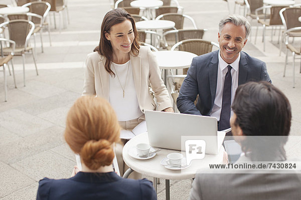 Lächelnde Geschäftsleute mit Laptop-Treffen im Straßencafé