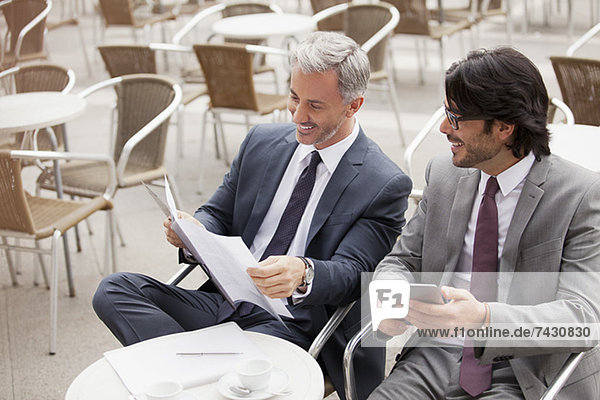 Smiling businessmen with digital tablet and paperwork in cafe