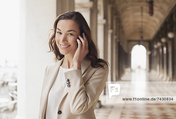 Porträt einer lächelnden Geschäftsfrau  die auf dem Handy im Flur spricht.