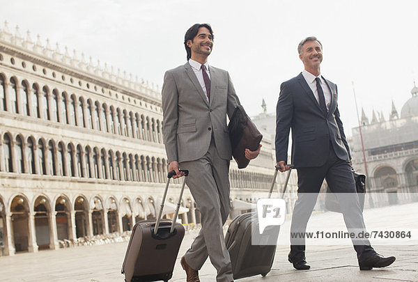 Smiling businessmen walking with suitcases through St. Mark's Square in Venice
