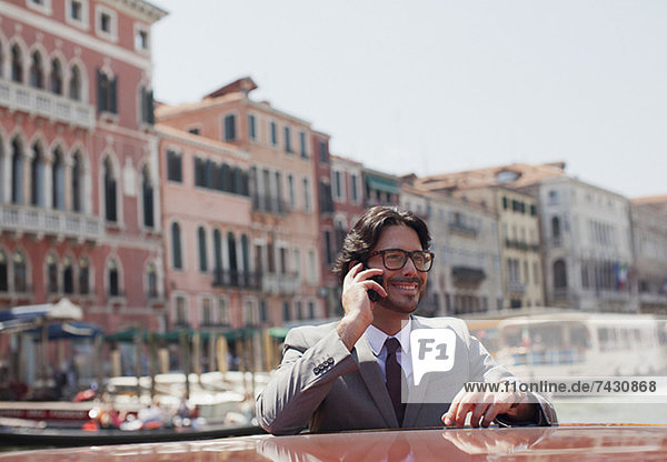 Lächelnder Geschäftsmann beim Telefonieren auf dem Schiff in Venedig