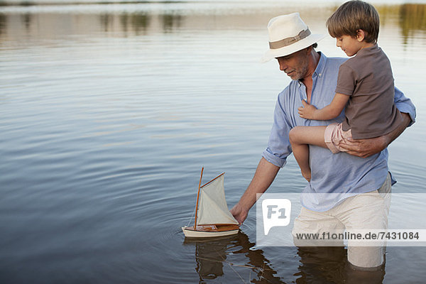 Großvater und Enkel watend im See mit Spielzeug-Segelboot